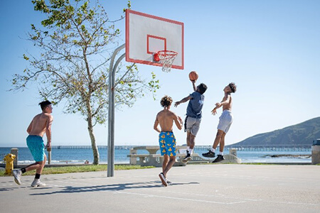 Group of teen boys playing basketball outside on sunny day.