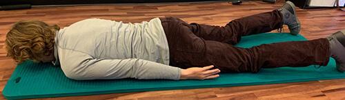 Man lying face down on an exercise mat with arms stretched behind at his sides