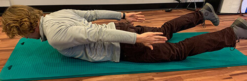 Man lying on his stomach on an exercise mat and lifting head and feet with arms stretched behind at his sides