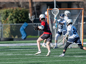 A high school lacrosse player running across the field. 