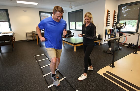 A man is running through an agility ladder drill while a therapist is beside with a stopwatch