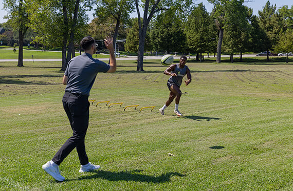 A therapist is outside throwing a football to an athlete that is running towards the ball