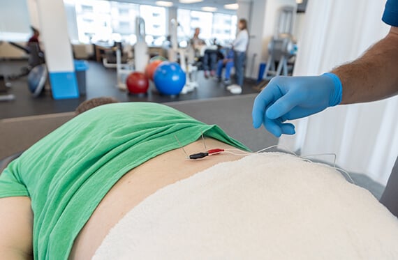 Close up of a patient's back as a therapist places two dry needles and an electrical current on the patient